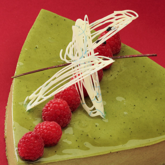 A slice of our Green Tea Kilo cake topped with white chocolate swirls and raspberries